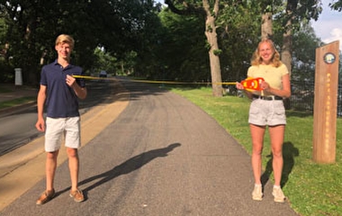 Students on a paved trail holding a tape measure showing that they are six feet apart. 