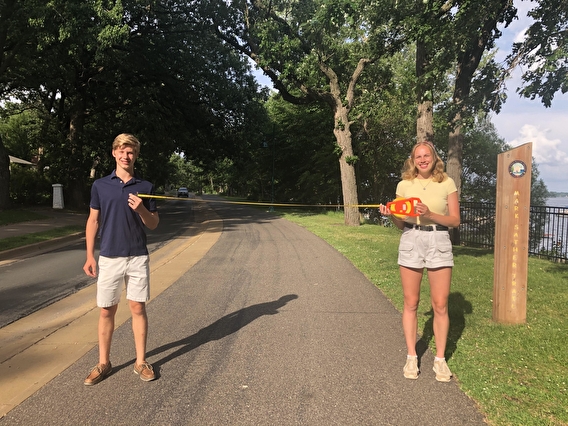 Students on a paved trail holding a tape measure showing that they are six feet apart. 