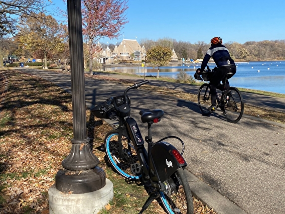 Bicyclist riding on a paved trail by a lake in the autumn