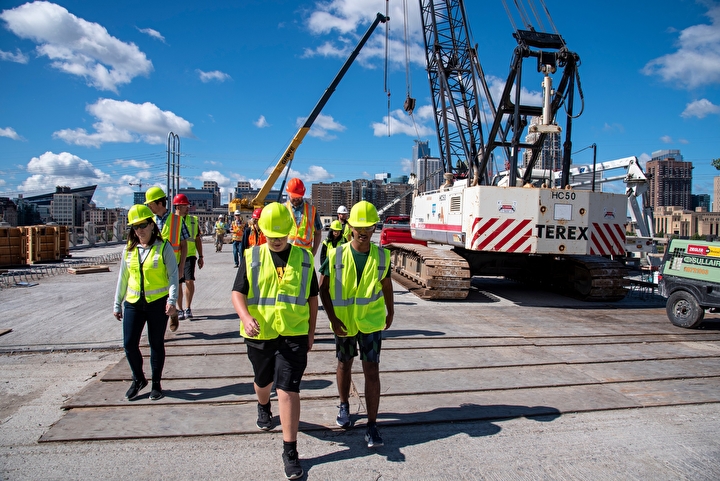 Students in safety vests and hard hats walking through a construction site